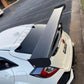 A white car with a large 9livesracing Civic Type-R Wang kit 2017+ FK8 carbon fiber rear spoiler is parked near a curb in a mostly empty parking lot. The car features black accents, including a prominent rear diffuser and window visors, optimizing its lift-to-drag ratio for increased down-force. The surrounding area shows some grass and a nearby building.