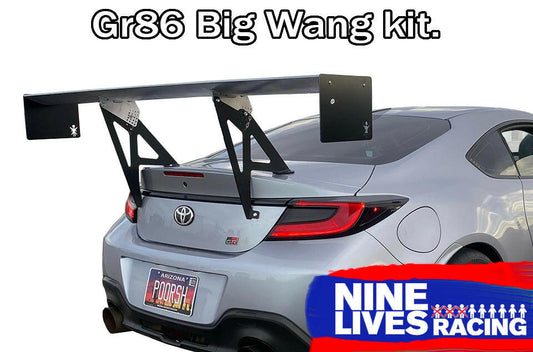 A silver Toyota GR86 is shown from the rear with a large aftermarket wing installed. The text "GR86 / BRZ Wang Kit '22+" is displayed at the top, and "9livesracing" appears at the bottom in a banner with a blue and red color scheme. Featuring extruded aluminum wings, it's designed for an optimal lift-to-drag ratio. The license plate reads "POORSH".