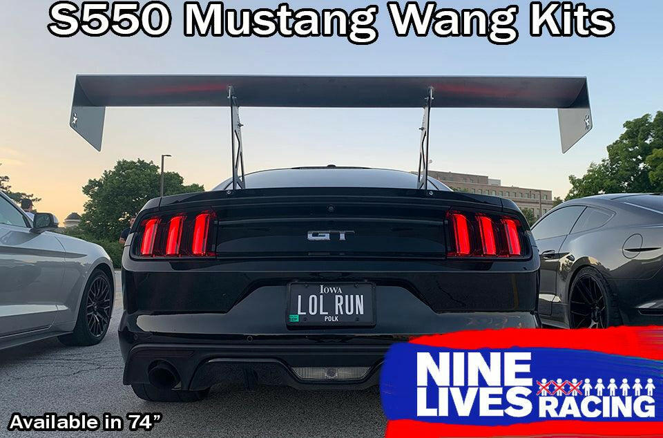 Rear view of a black GT Mustang equipped with a large Mustang Big Wang Kit '14+ S550 from 9livesracing, enhancing Mustang performance with its impressive down-force. A license plate reads "LOL RUN." The car is parked next to other vehicles. The image includes text: "S550 Mustang Wang Kits," "Available in 74"" and "Nine Lives Racing" with the brand's logo.